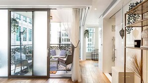 Un interior moderno con un puertas corredera de vidrio que da a una zona de estar exterior, suelo de madera y una vitrina de vidrio con objetos decorativos.