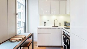 Una cocina compacta con gabinetes blancos, un lavamanos y una estufa. Se aprecia una ventana que proporciona luz natural y vistas de la ciudad.