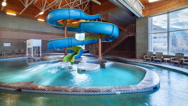 Una piscina coperta con diversi scivoli, un muro in mattoni e vista su edifici esterni.