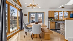 Une cuisine moderne avec des meubles en bois, un coin repas doté d’une grande table et de chaises, et de grandes fenêtres offrant une vue sur l’extérieur.