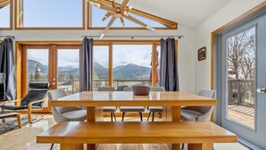 Une pièce spacieuse avec une grande table à manger en bois, de nombreuses chaises et une vue sur les montagnes grâce à de grandes fenêtres.