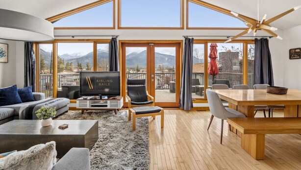 Un salon spacieux doté d’un grand téléviseur, de sièges confortables, d’un coin repas et offrant une vue sur les montagnes grâce à de grandes fenêtres.