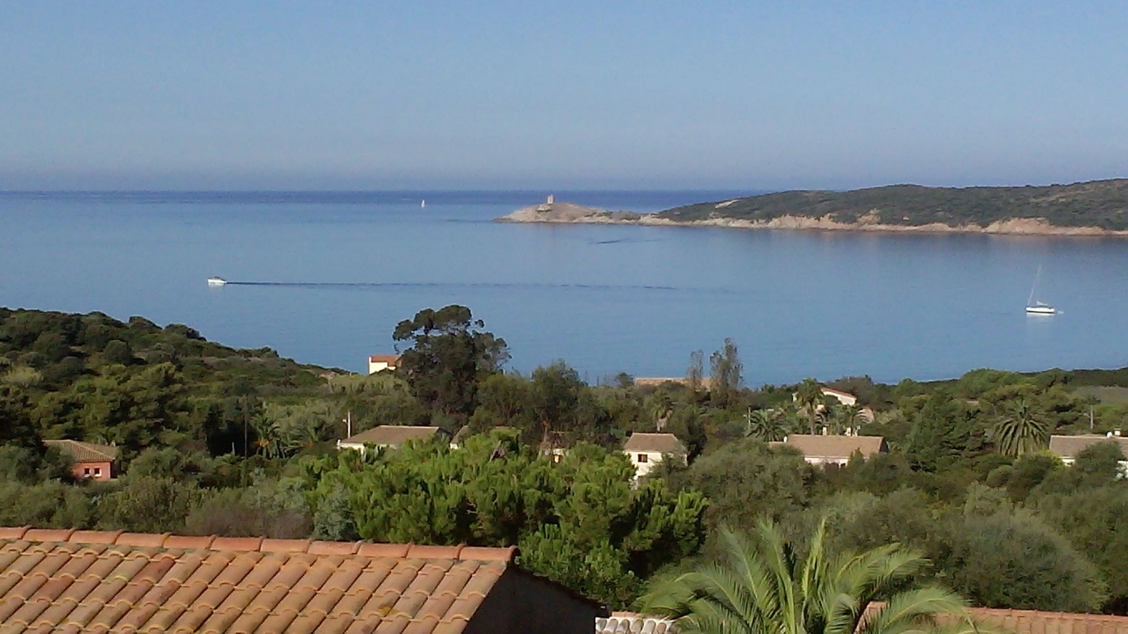 Vista costeira com casas, um farol e barcos na água.