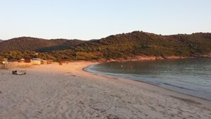 A beach with a sandy shore, a small building, and a hill in the background. - Air-conditioned apartment with sea view, in a residence in the heart of a 3-hectare park (Cargèse)