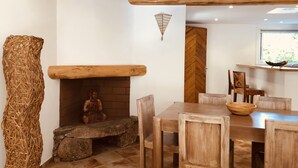 A dining area with a rustic wooden table and chairs, a stone bench, and a Buddha statue by a brick fireplace. - Charming*** villa with heated pool, close to town center (Porto-Vecchio)