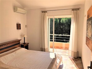 A bedroom with a large bed, an air conditioning unit, a bedside table with a lamp, and a view of the outdoors through a sliding glass door. - Charming *** Villa with a Heated Pool, Near the City Center (Porto-Vecchio)