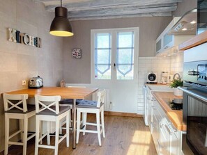 A modern kitchen with white cabinets, a wooden dining table, and a hanging light fixture.