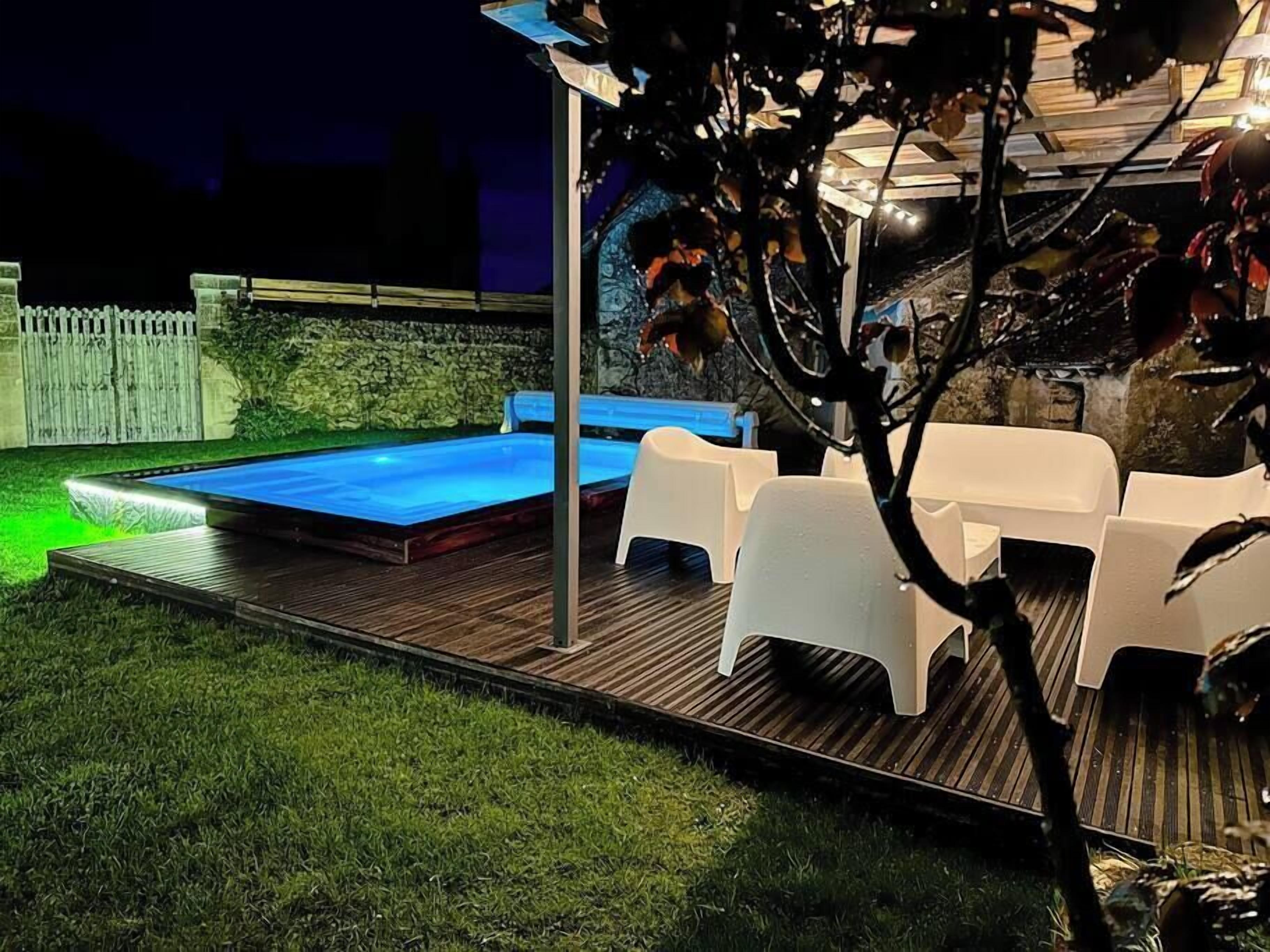 Un espace extérieur abrité comprenant une piscine, des chaises en plastique blanches et une terrasse en bois.
