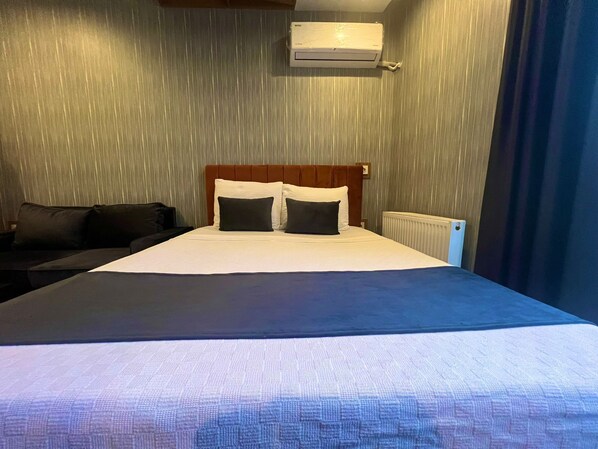 Quarto de hotel com cama, cabeceira, mesa de cabeceira e ar condicionado fixado na parede.
