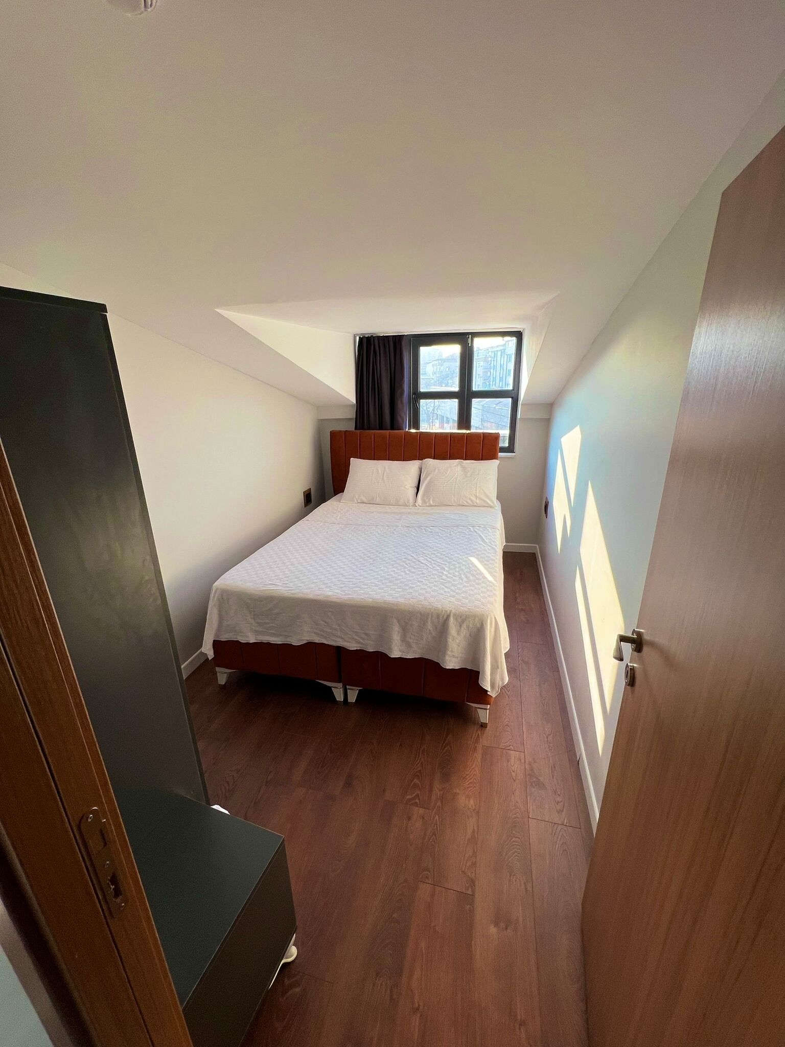 Un dormitorio con cama, ventana con cortinas y puerta.