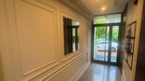 A hallway with a polished stone floor, white wainscoting, and a door leading outside. - Beta Hotel (Istanbul)