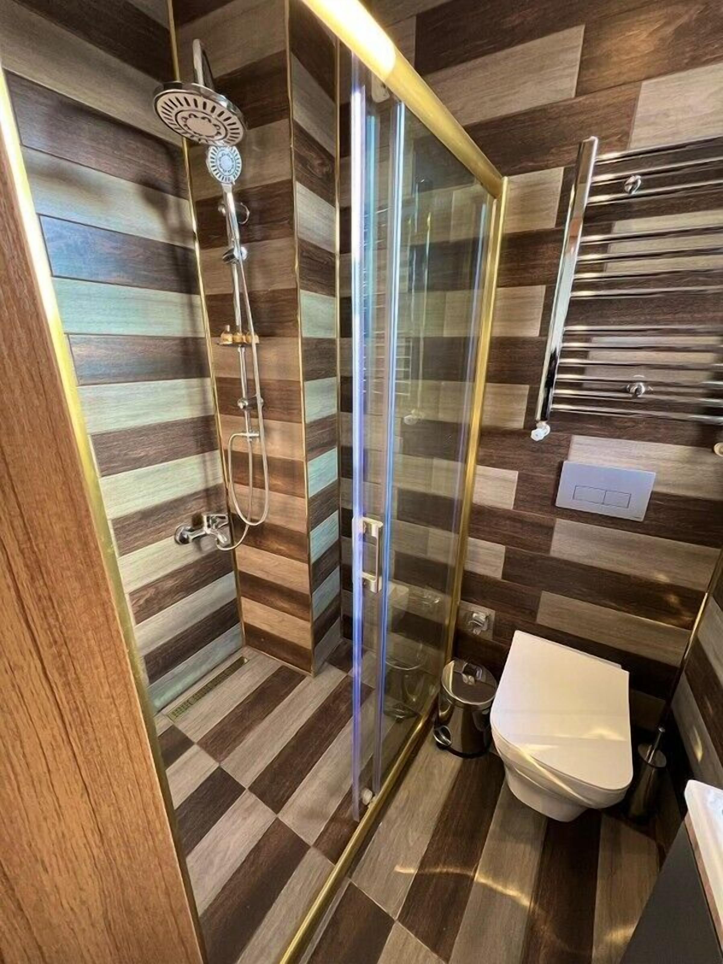 A modern bathroom with a glass-enclosed shower, a toilet, and a towel rack.