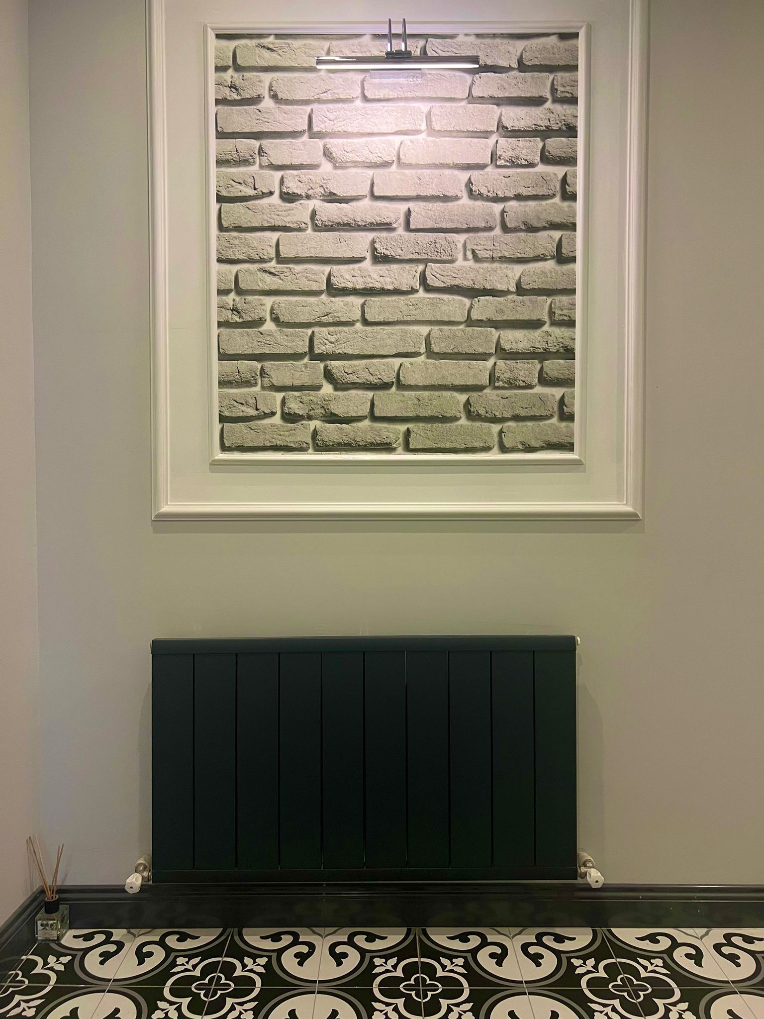 A room with a brick-patterned wall, a radiator, and patterned floor tiles.