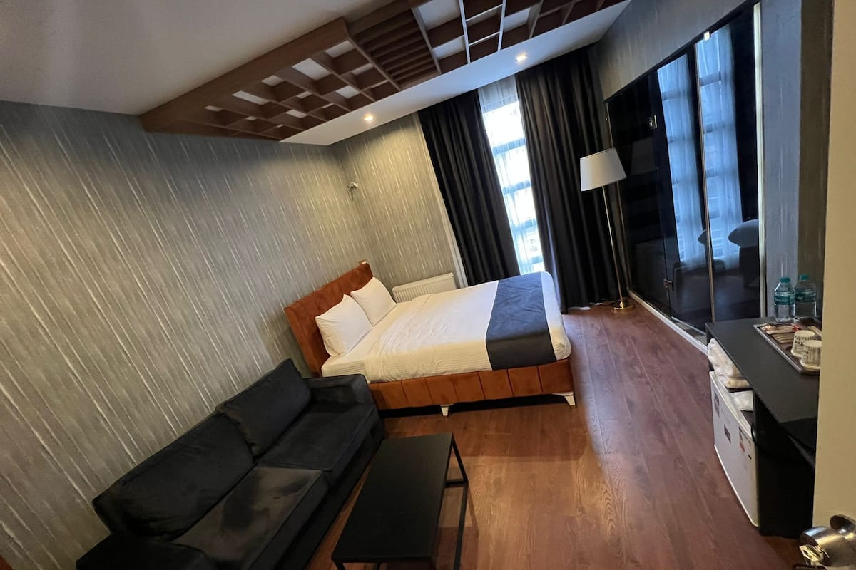 A modern hotel room with a bed, a black sofa, a small table, and a TV.