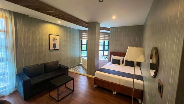 A hotel room with a bed, a sofa, a small table, and a lamp. - Beta Hotel (Istanbul)
