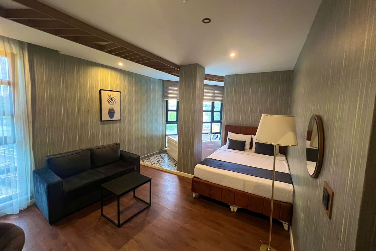 A hotel room with a bed, a sofa, a small table, and a lamp.