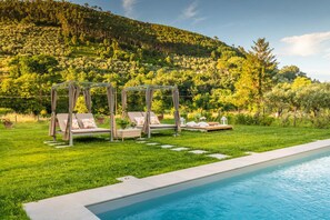 A poolside area with a pergola, two lounge chairs, and a small table with a lantern. - Villa Ester in Capannori (Capannori)
