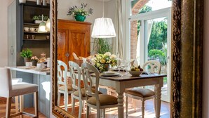A dining area with a table set for four, surrounded by white chairs. A wooden cabinet with shelves is visible to the left, and a large mirror hangs on the wall. - Villa Ester in Capannori (Capannori)