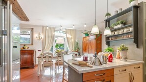 A modern kitchen with a central island, wooden cabinets, and a built-in shelf with plants. - Villa Ester in Capannori (Capannori)