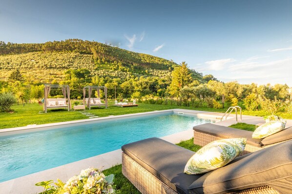 A swimming pool with lounge chairs and a pergola, surrounded by lush greenery and hills. - Villa Ester in Capannori (Capannori)