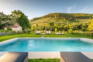 A rectangular swimming pool with a clear blue water surface, surrounded by a well-maintained grassy area and a wooden pergola with cushions. - Villa Ester in Capannori (Capannori)