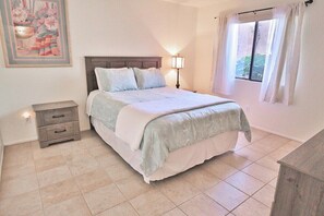 A bedroom with a bed, bedside table, lamp, and a window with curtains.