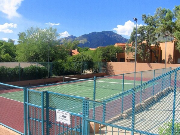 Ein Tennisplatz mit einem Schild an einem verschlossenen Pooltor, umgeben von Grünflächen und Gebäuden.