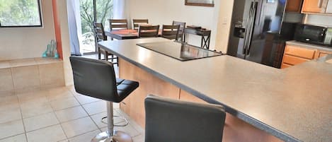 Una cocina moderna con una isla grande, taburetes de bar, un refrigerador y un comedor con sillas y una mesa.