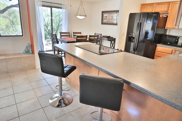 A modern kitchen with a large island, bar stools, a refrigerator, and a dining area with chairs and a table.