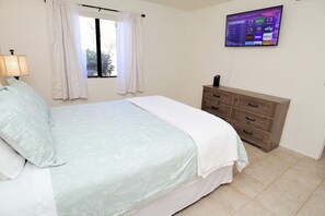 A bedroom with a bed, a dresser, a TV mounted on the wall, and a window with curtains.