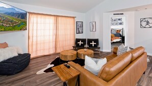 A modern living room with a brown leather sofa, two black chairs with white crosses, a wooden coffee table, and a large window with curtains. - Spectacular Music Lovers Condo (Palm Springs)
