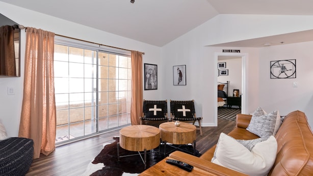 A modern living room with a leather sofa, two wooden chairs, a coffee table, and a remote control on it. - Spectacular Music Lovers Condo (Palm Springs)