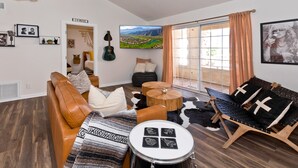 A living room with a brown leather sofa, a drum, a black and white patterned rug, a wooden coffee table, and a black lounge chair with a cowhide rug. - Spectacular Music Lovers Condo (Palm Springs)