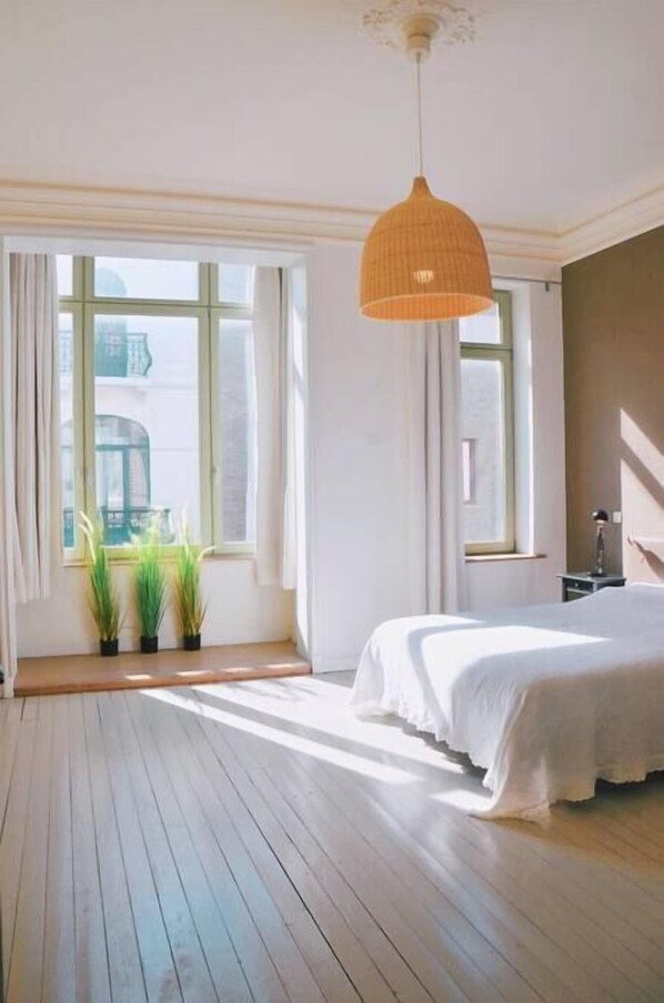 A bedroom with a large window, a bed, and a hanging light fixture.