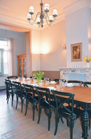 A dining room with a wooden table set for six, surrounded by black chairs, a chandelier, and a fireplace with a vase of flowers.