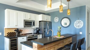 A modern kitchen with white cabinets, stainless steel appliances, a wine cooler, and a bar area with stools. - Southern Star Villa Kayaks, SUPS, Steps to Beach (Cruz Bay)