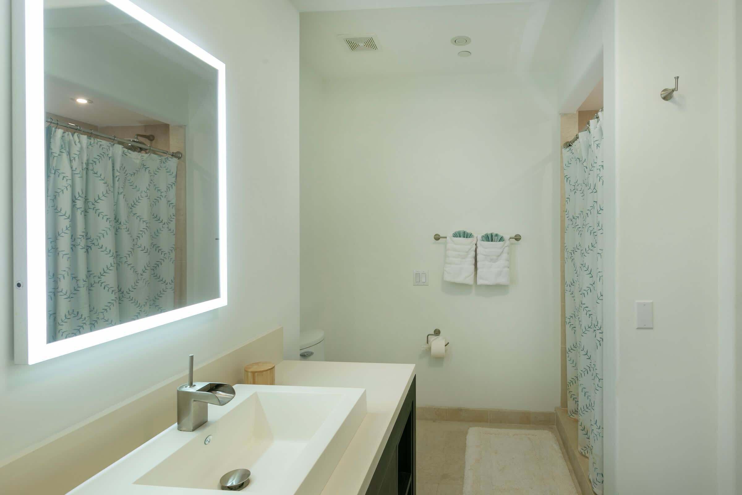 A modern bathroom with a large mirror, a sink, a shower, and a toilet.