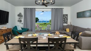 A dining area with a wooden table, chairs, and a view of the sea through large windows. - Southern Star Villa Kayaks, SUPS, Steps to Beach (Cruz Bay)