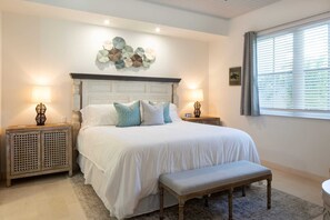 A bedroom with a large bed, two bedside tables, a bench, and a decorative wall piece. - Southern Star Villa | Kayaks & Beach | by BookVI (Cruz Bay)