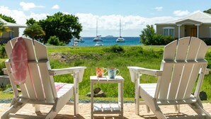 Two white Adirondack chairs facing a view of the sea with sailboats, a small table with two cups, and a house in the background. - Southern Star Villa Kayaks, SUPS, Steps to Beach (Cruz Bay)