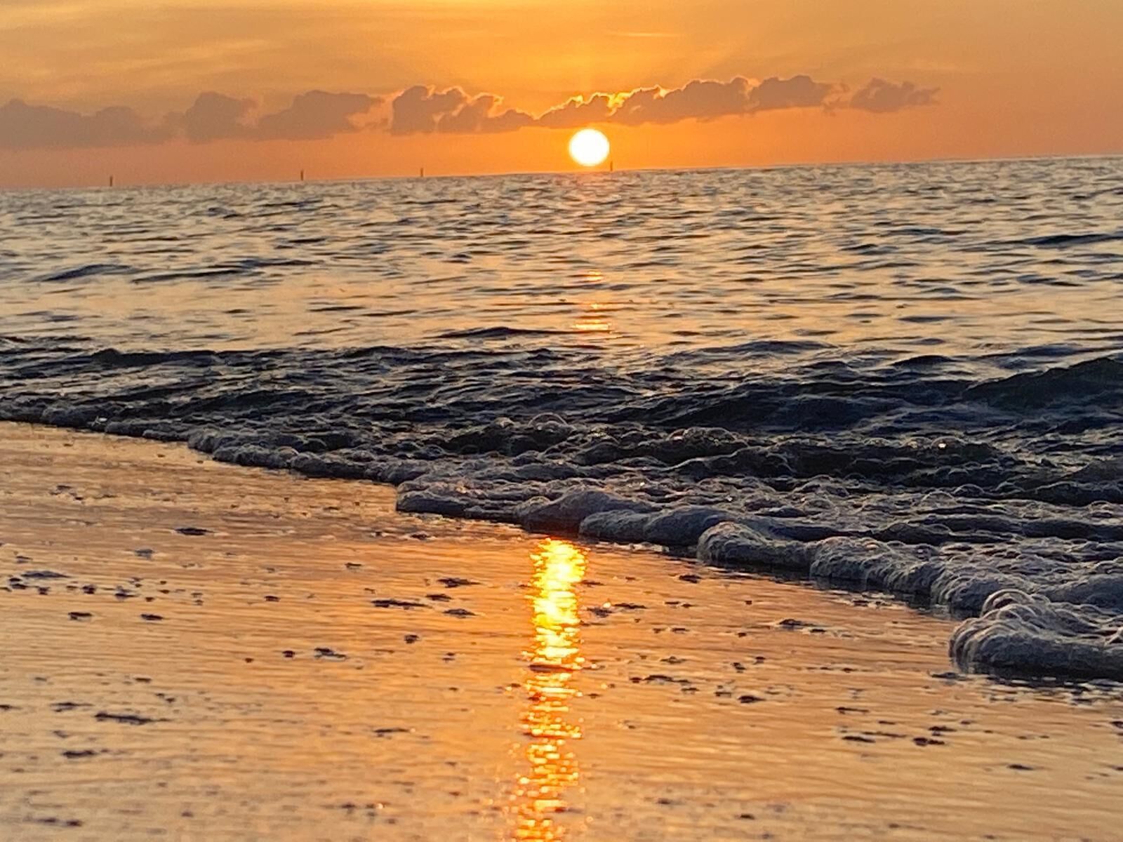 A sunset over the ocean with waves approaching the shore.