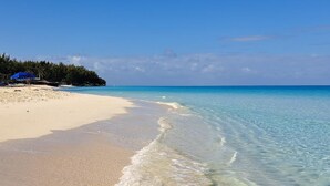 Una platja amb aigua turquesa cristal·lina, sorra daurada i una zona boscosa al fons.