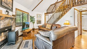 Ein gemütliches Wohnzimmer mit einem Kamin aus Stein, einer bequemen Ledersofa, einer Holztreppe und einem großen Fenster mit Jalousien.