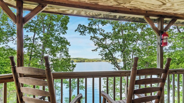 Eine Holzterrasse mit zwei Stühlen mit Blick auf einen See, umgeben von Bäumen.