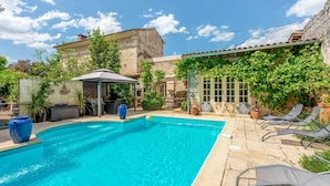 Una piscina con sillas de descanso, una zona de estar cubierta y un edificio de piedra con vegetación.