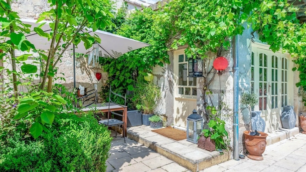 Un patio con una mesa y sillas, rodeado de abundante vegetación y muros de piedra.