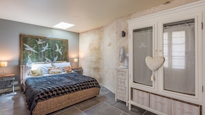 Un dormitorio con una cama grande, un ventilador de pared, un armario con un espejo con forma de corazón y un cuadro de pájaros en la pared.