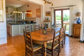 Een eetgedeelte met een houten tafel en stoelen, een keuken op de achtergrond en uitzicht op het buitenlands gebied door een glazen deur.