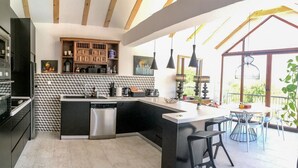 Una cuina moderna amb una illa central, respatller amb dibuixos en blanc i negre, i una zona de menjador amb taula i cadires.