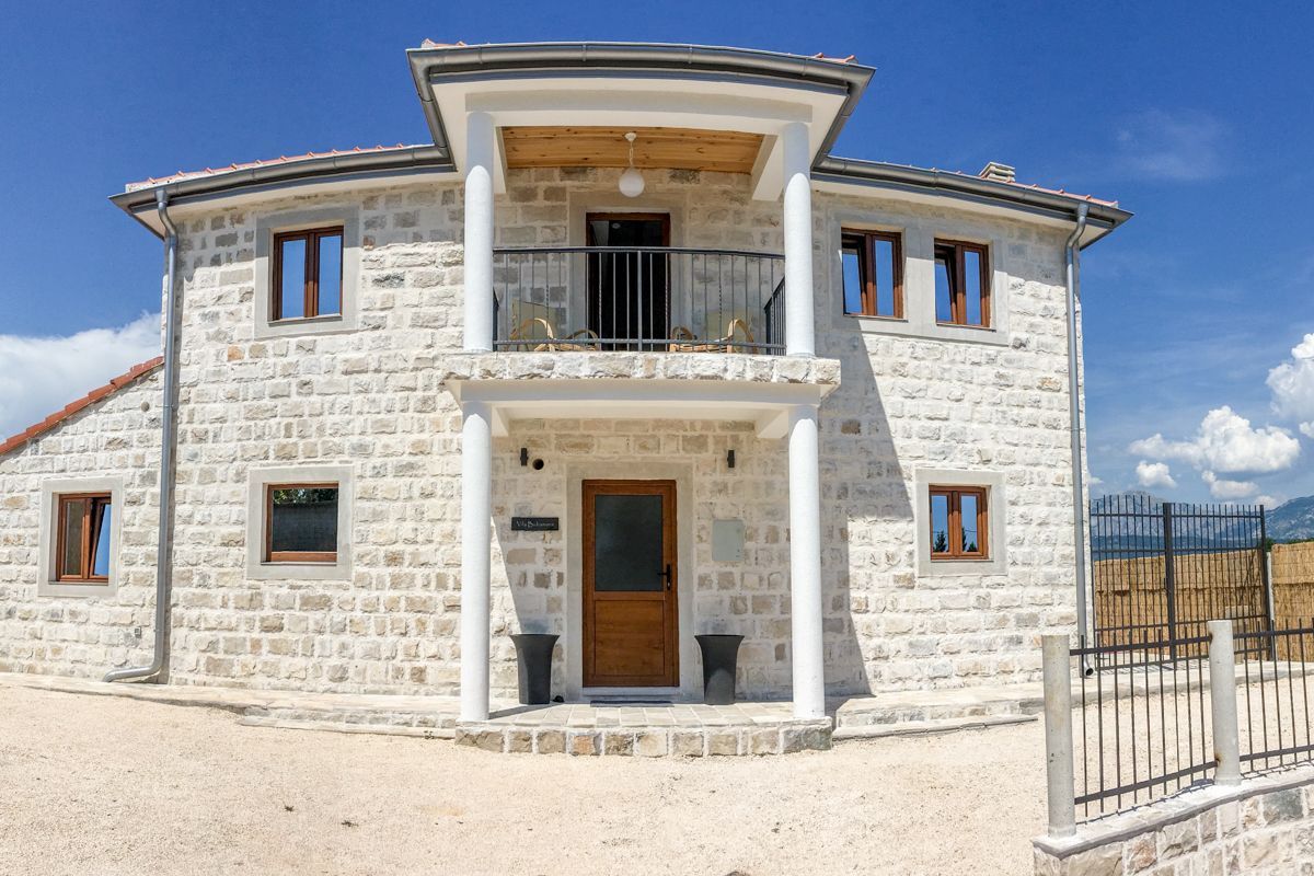 A two-story stone building with a wooden door, a balcony, and a fenced yard.